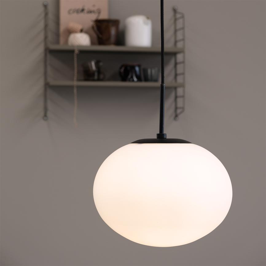 The lamp: a round, white pendant, hangs lit and casts soft light; behind wall shelf with jars, cups and a book with the text "cooking".