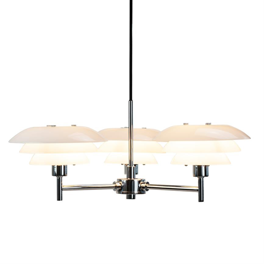 A chrome pendant hangs and emits soft, warm light from three layered white shades; presented against a neutral white studio background.