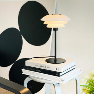 The lamp is lit on a stack of books (THE KINFOLK HOME; ARA GULER'S Istanbul) on a small white stool in front of a wall with large black circles.