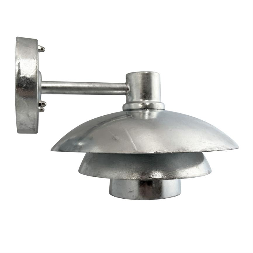 Silver metal wall lamp with three layered round shades is mounted on a short arm and points downwards against a neutral white background.