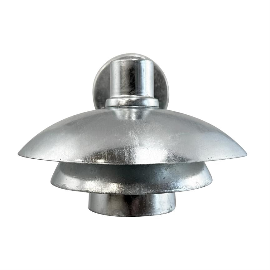 Silver metal wall lamp with three layered, bowl-shaped shades; mounted on a round wall plate; photographed against a uniform white background, studio lighting highlights the matte metallic sheen.