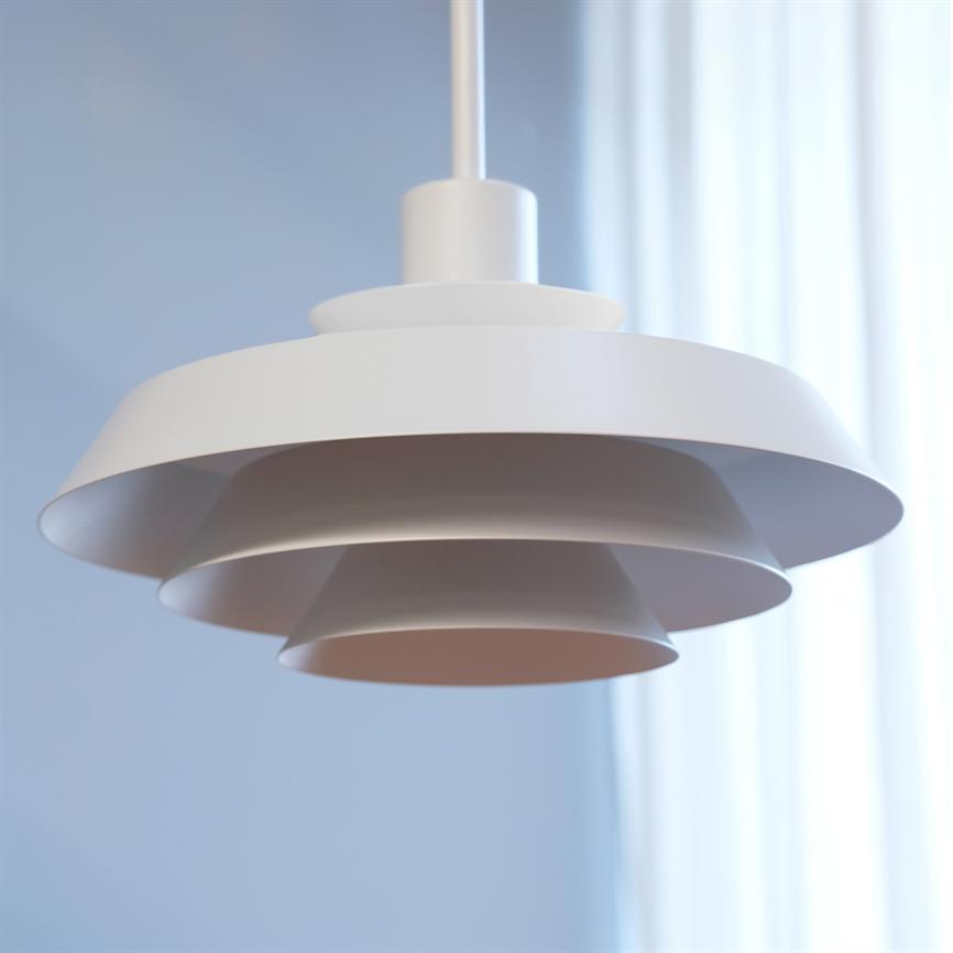 A white, layered pendant light hangs quietly from the ceiling; its circular screens overlap. The background shows a soft blue wall and bright, translucent white curtains.