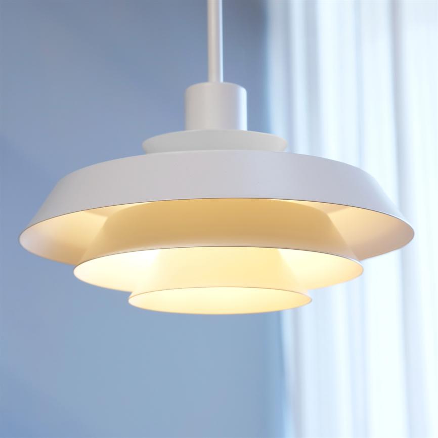 A white, multi-layered ceiling lamp hangs and emits warm, diffused light over a room with pale blue walls and an almost transparent white curtain in the background.