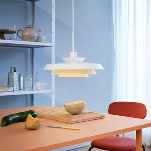 A white one pendant lights above an orange table; a melon half on a cutting board, a zucchini next to it, with a red chair and shelf in the background.