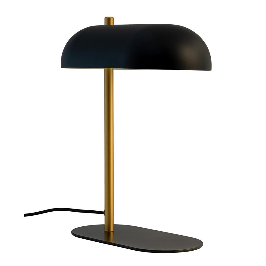 Black and brass table lamp stands on a flat oval black base; a narrow brass rod leads up to a hemispherical black screen, in front of a white, neutral background.