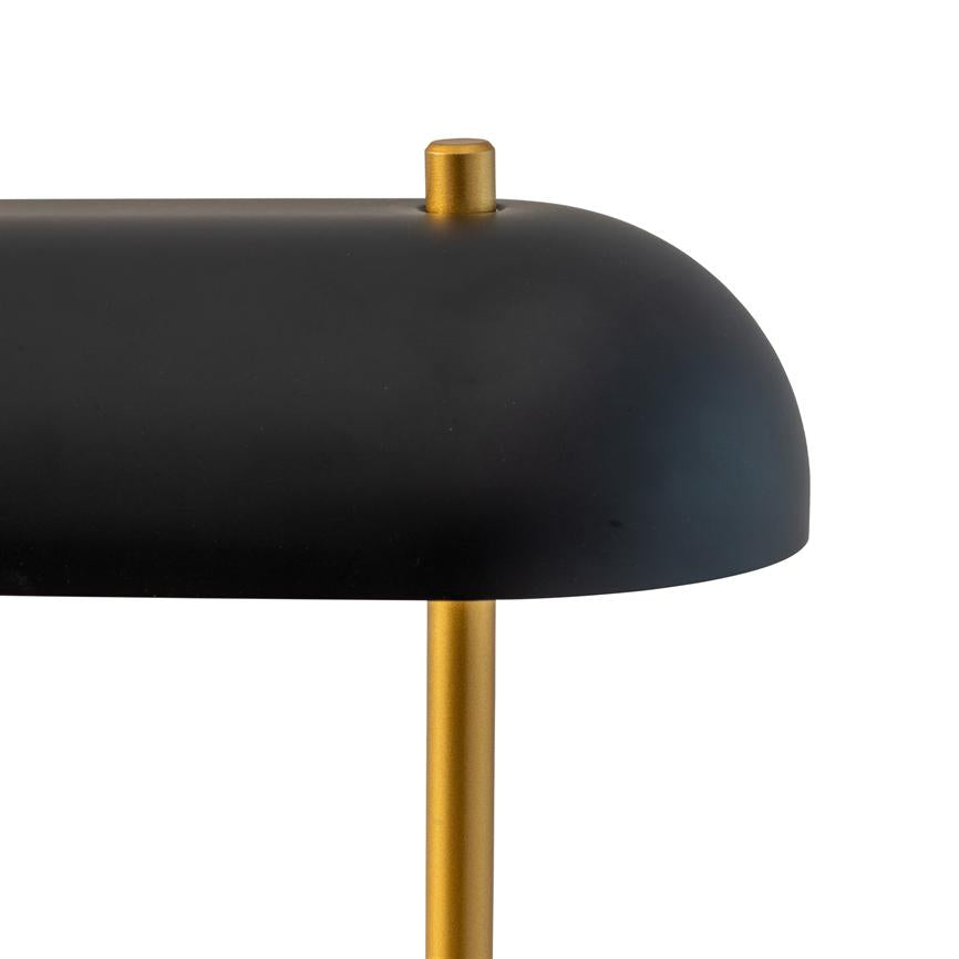 Black, curved lampshade with small gold-colored knob rests on a slender gold-colored rod against a clean, white background.