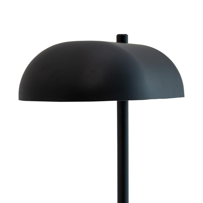 Black table lamp with hemispherical shade stands on a slender vertical pole; matte surface, minimalist design against a uniform white background.