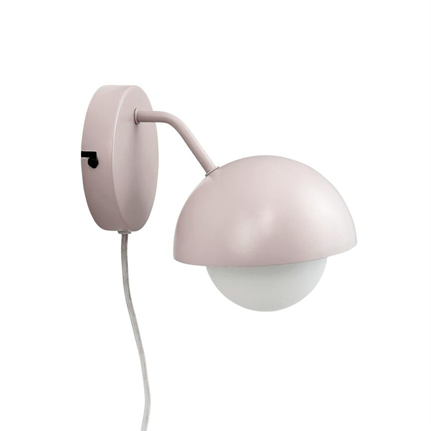 Wall lamp with pink matte half shade enclosing a white round bulb; arm arches from a round wall plate, with visible fabric cable and black switch.