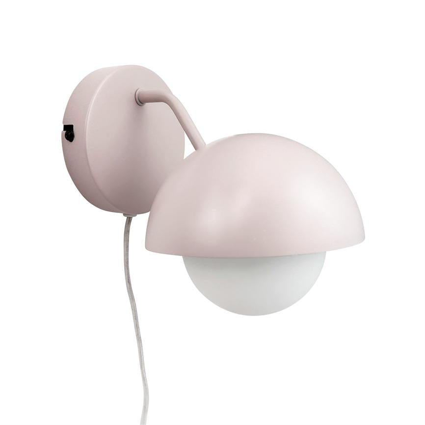 Wall-mounted lamp with matte pale pink dome shade resting above a round opal globe; curved arm connects to circular wall bracket with small black switch, textile cord hangs down on white background.