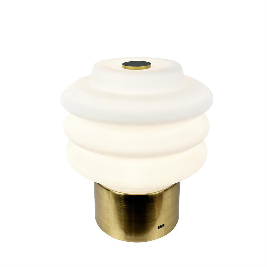 Table lamp with ribbed white opal glass dome, emits soft warm light; rests on cylindrical brushed brass base with small USB port, against neutral white background.