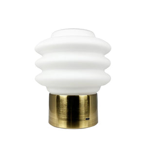 Table lamp: wavy, white opal glass dome sits on a brass-colored cylindrical base; the lamp is turned off and placed against a neutral white background; visible USB-C port at the bottom.