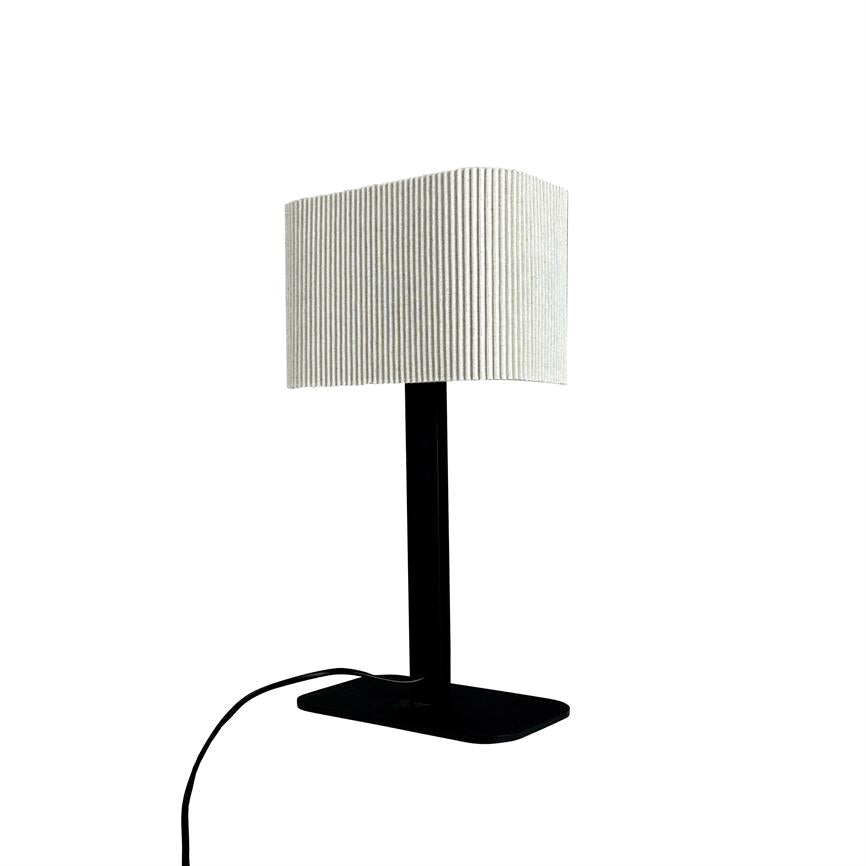 Table lamp stands vertically on a black, flat base; a black pole supports a white, wrinkled cylindrical lampshade. Black wire lies bent at the foot on a uniform white background.