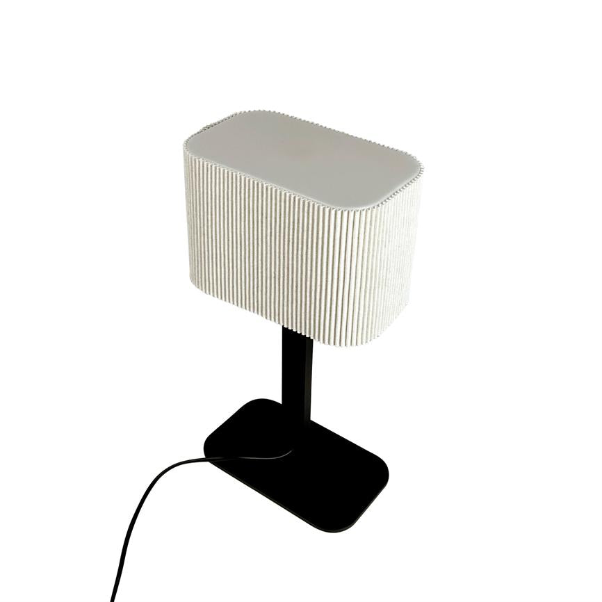 Table lamp with rectangular, ribbed white shade sits on a black rod and foot; black wire runs from base on white background.