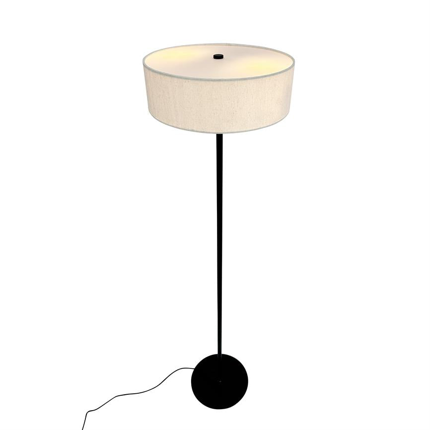 A floor lamp emits soft, warm light in a simple white background; it has a tall, slim black pole, round black foot and a large beige cylindrical lampshade.