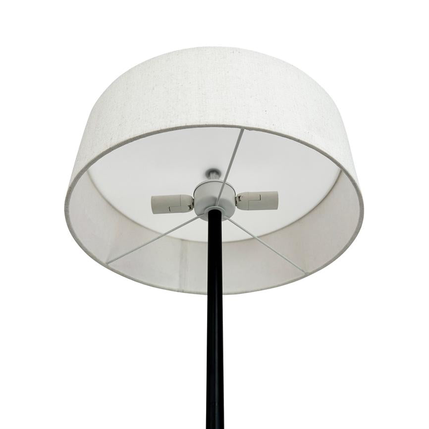 Floor lamp with white cylindrical fabric shade, seen from below; the screen's inner and metal radials and two sockets are visible, mounted on a black, vertical stand in a bright, neutral room.