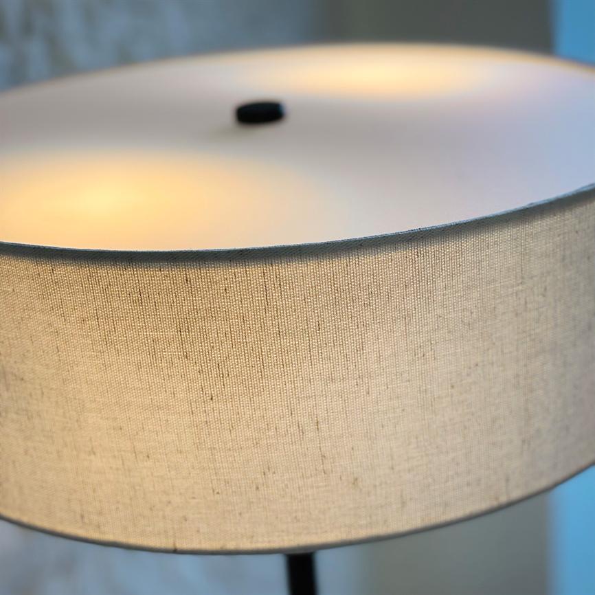 A round, beige fabric lampshade emits warm, diffused light through the texture; it has a black knob at the top and is closely cropped against a soft, neutral background.