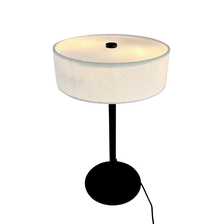 Table lamp with round, white fabric shade that emits warm, soft light; thin black rod and round black foot, with visible black power cord, photographed on a white background.