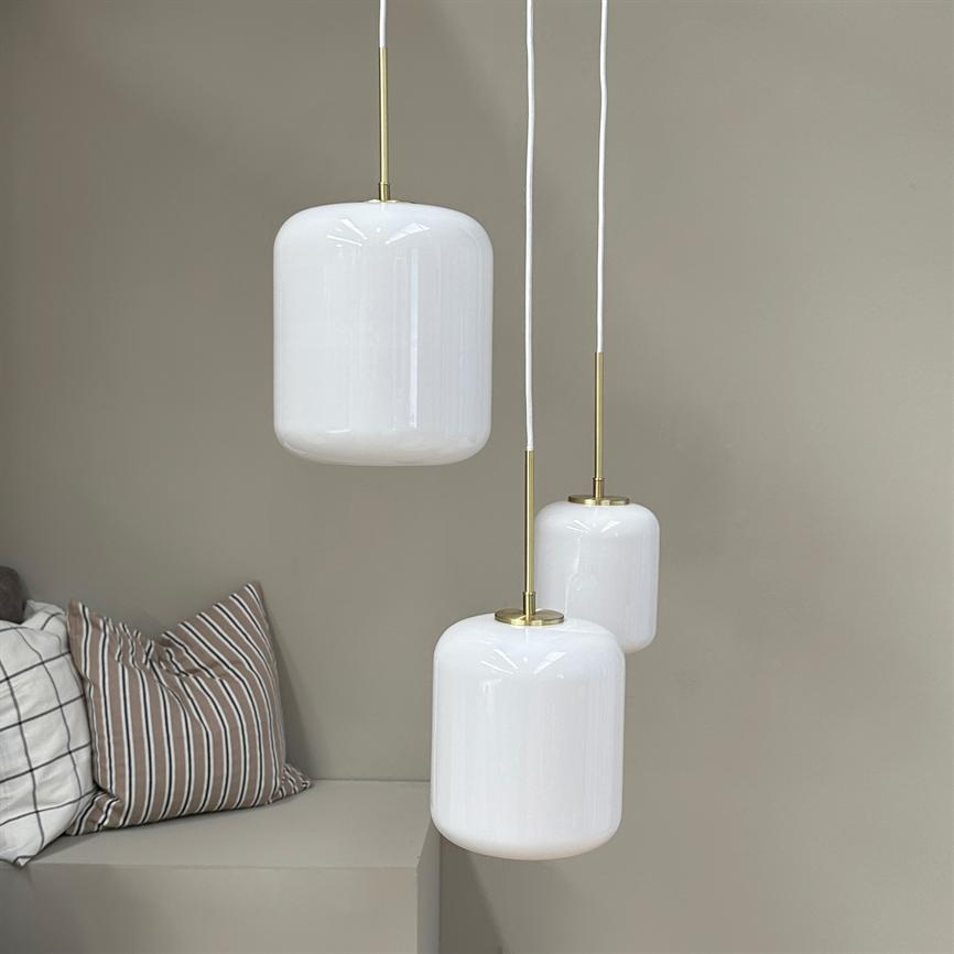Three white glass pendants hang at different heights from white wires and brass fittings; in front of a beige wall above a built-in bench with striped and checked cushions.