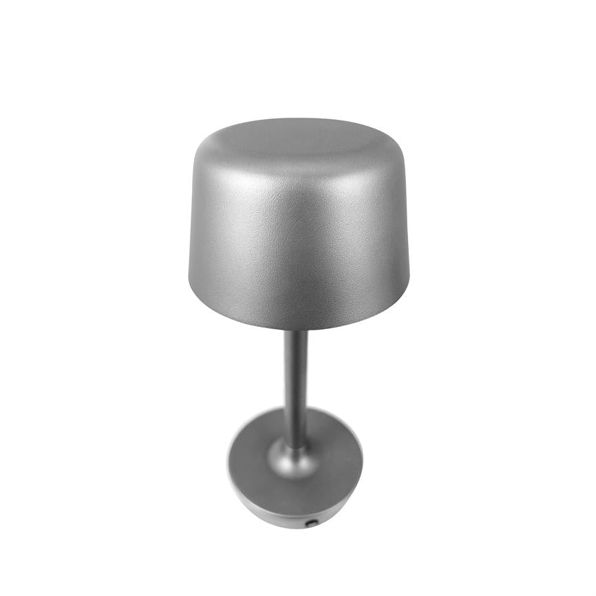 Silver table lamp standing upright on white background; a slender stem connects a rounded cylindrical shade and a round base, matte metal finish, photographed from above.
