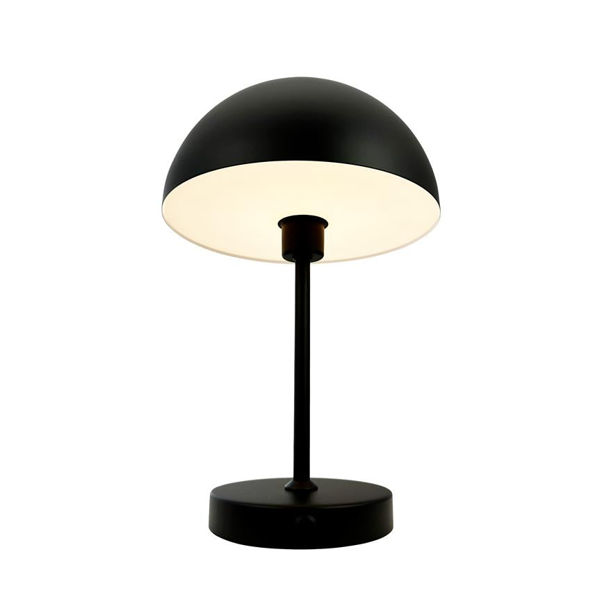 A table lamp with a black dome shade shines softly downwards; mounted on a slim black pole and round base, isolated against a neutral white background.