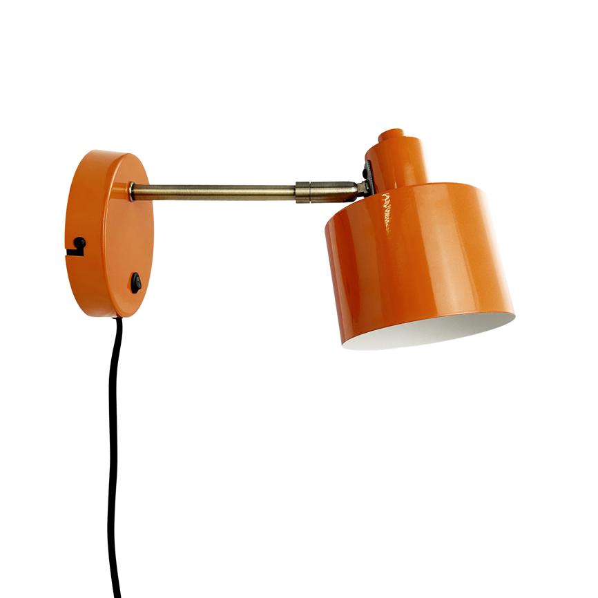 Orange wall lamp tilted to the right; lamp head is mounted on a short brass arm and a round wall bracket, black cord hangs down in front of a white background.