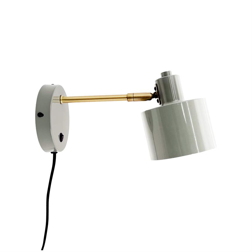 Wall lamp with round wall mount and brass arm, adjustable white cylindrical shade points obliquely downwards; black wire hangs down from the bracket against a clean white background.