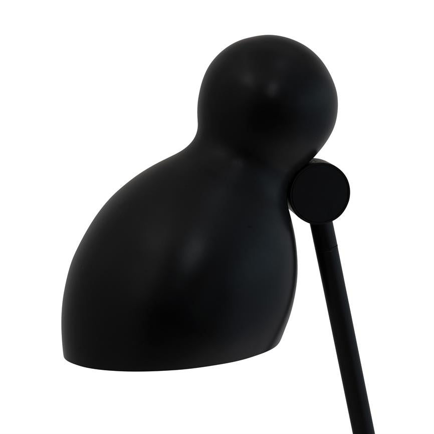 Black, rounded lamp head tilts slightly forward on a thin rod, directed downwards over a clean, white background; minimalist, matte surface.