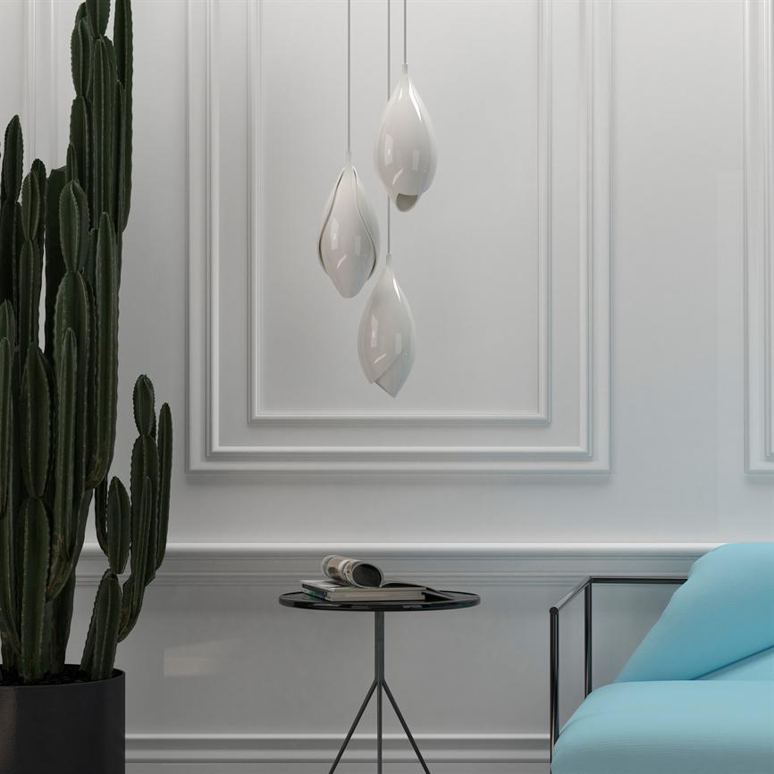 Three white, drop-shaped pendant lamps hang above a round side table with an open book; surrounded by profiled white wall panels, a tall cactus on the left and a pale blue sofa on the right.