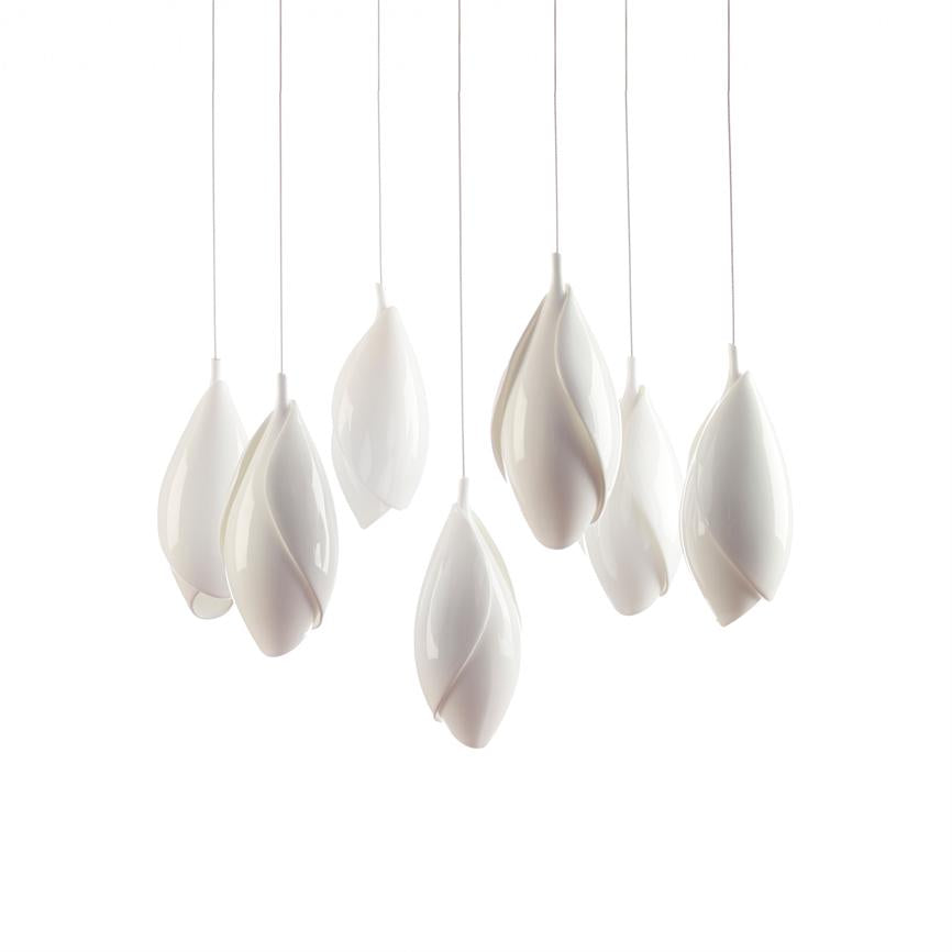 Seven white, graft-like pendant lamps hang from thin cables, floating lightly at different heights above a neutral, white background, with a glossy, smooth surface and soft, organic shapes.
