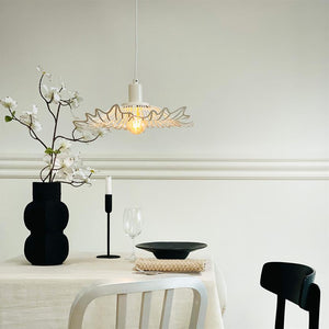A white decorative hanging lamp casts a warm light over a covered table; a black vase with white flowers, one candle, wine glass and black plate in a minimalist, light gray dining room.