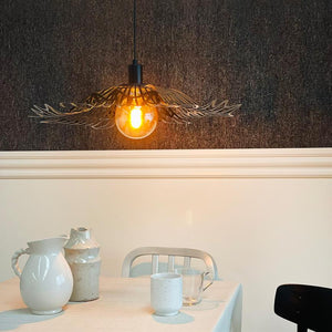 A decorative hanging lamp casts a warm glow above a dining table; the table has white ceramic jugs and mugs, in front of white paneled wall and dark textured wallpaper.