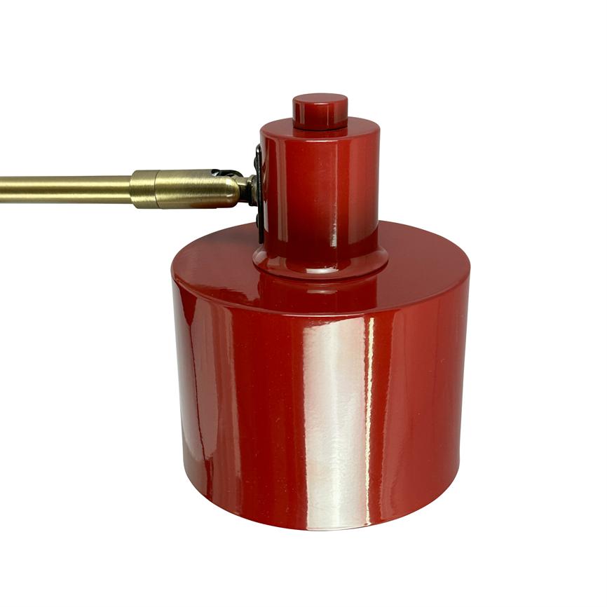 Red cylindrical lampshade mounted to a brass colored arm via a hinge; glossy, reflective lacquer surface shows light reflections. White background.