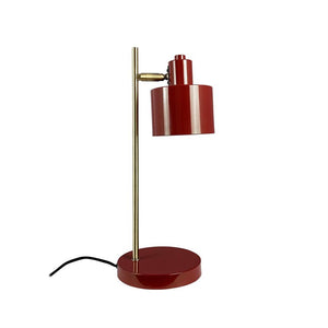Table lamp in red metal with golden rod, shade directed downwards, standing on round red base; black power cord lies next to it on white background.