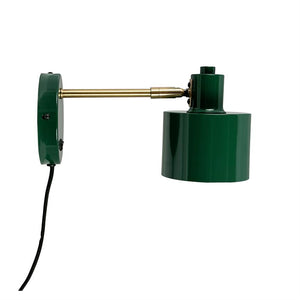 Green metal wall lamp extends a brass arm and hangs with a cylindrical shade against a white background; black fabric cable leads downwards.