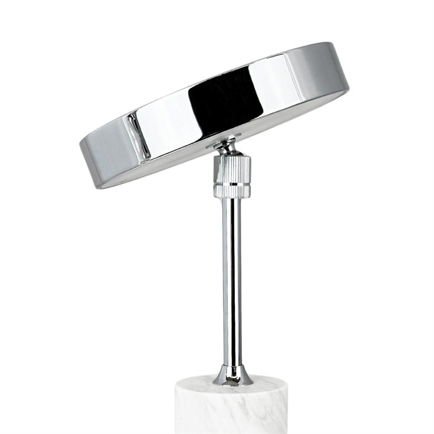 Round chrome-plated cosmetic mirror tilts forward on an adjustable joint, mounted on a slim chrome rod, standing in a cylindrical white marble base against a white background.