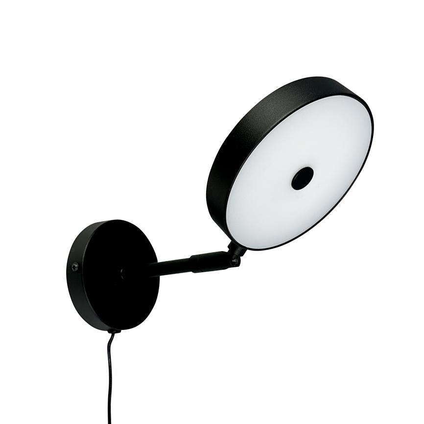 Round wall lamp with black metal frame and white diffuser; tilted outwards on a short arm from a round wall plate, with visible black wire, against a neutral white background.