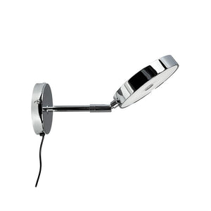 Chrome wall lamp extends an adjustable arm with a flat, circular lamp head, angled downwards; round wall bracket with visible black cord in front of white background.