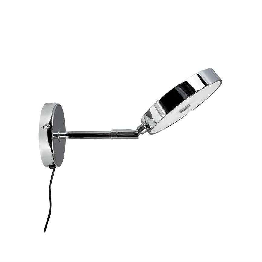 Chrome wall lamp extends an adjustable arm with a flat, circular lamp head, angled downwards; round wall bracket with visible black cord in front of white background.