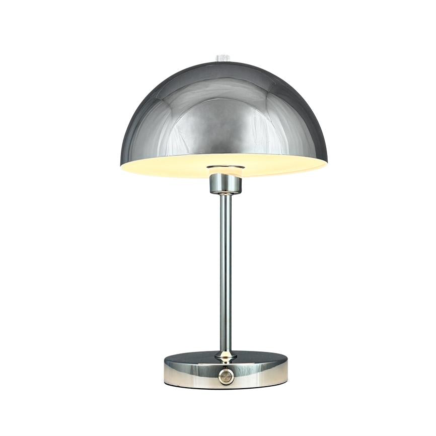 A chrome table lamp with a hemispherical shade shines warmly downwards; slim rod and round foot with push button stand on white background.