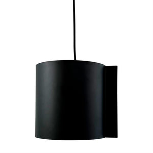 Black cylindrical hanging lamp hangs from a thin black cord, with a flat wall plate to the right, in front of a neutral white background.
