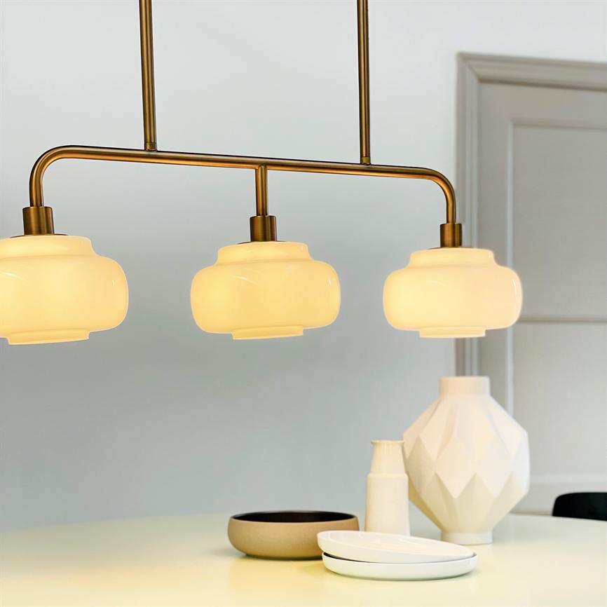 Three hanging opal glass lamps glow softly above a table with white vases, a bowl and plates in a bright, modern kitchen/dining room with gray walls and door frame.