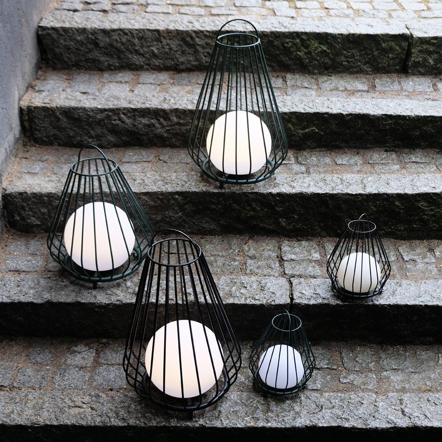 White globe lamps in open, cone-shaped metal cages are positioned on uneven gray stone steps outdoors; six lamps of various sizes arranged in a loose group along the steps.
