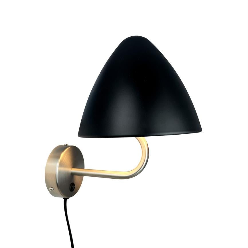 Wall lamp with black, conical shade sits on curved brushed metal arm, emits warm downward light; round wall plate mounted on white background, black cord hanging down.