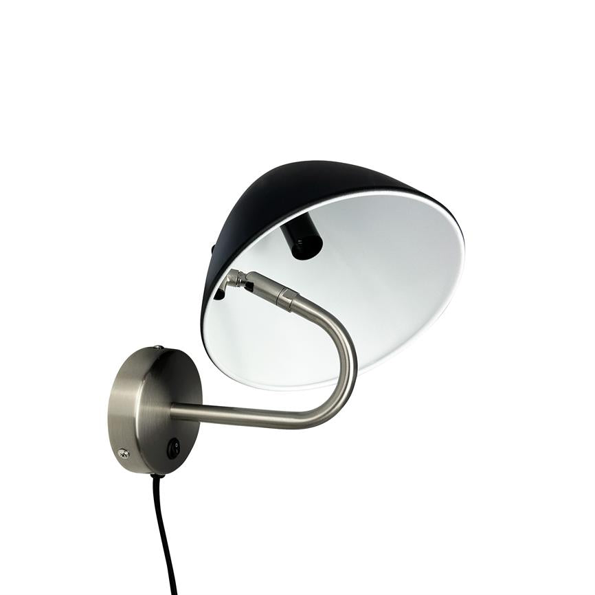 Wall lamp is mounted on a round metal plate, arm bent in S-shape holds a black lampshade with white inside; power cable hanging down against white background.