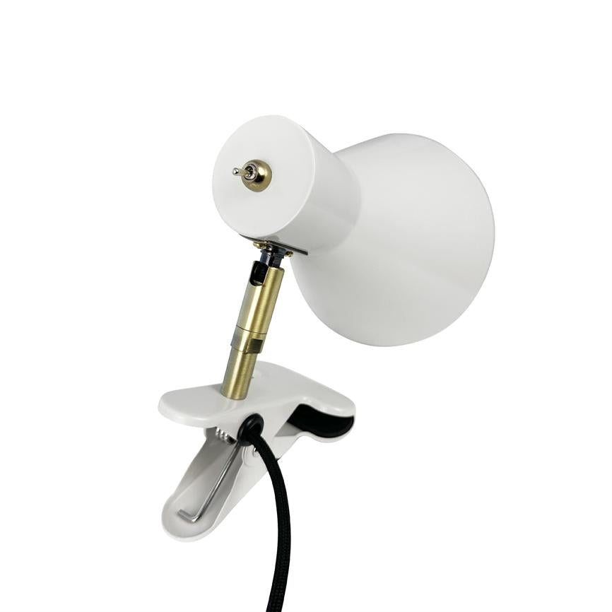 A white clamp-on table lamp clamps on, tilting its conical shade upwards via a brass-coloured joint/wire piece; a black fabric cord hangs down in front of a neutral white background.