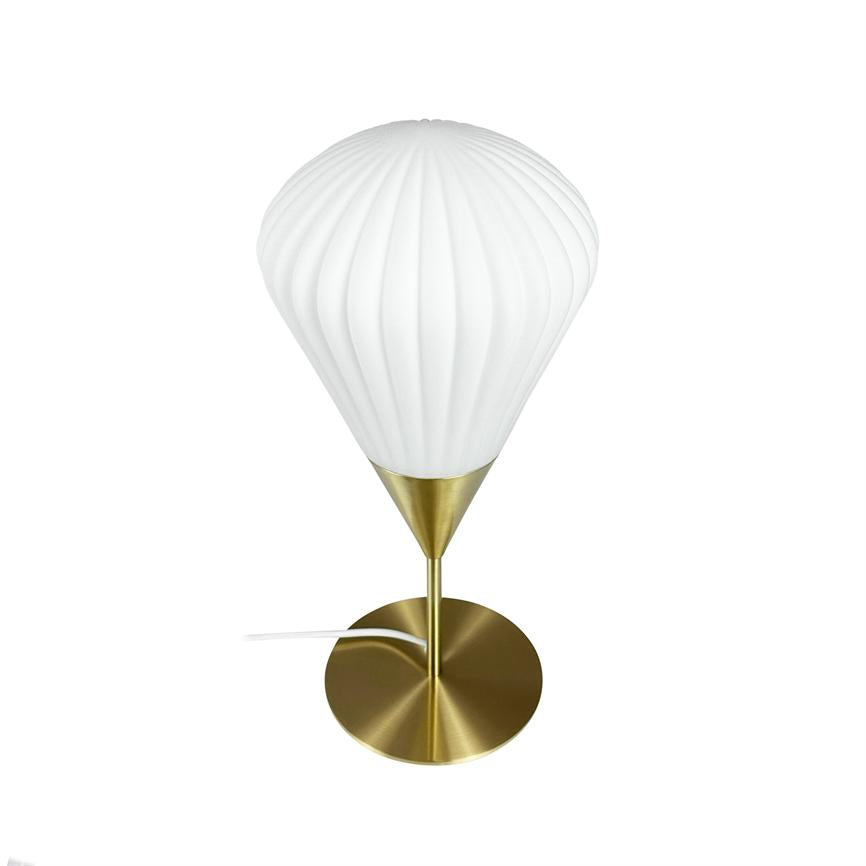 En bordlampe med hvid, ribbet skærm hviler på en konisk messingholder, som står på en rund, børstet messingfod; hvid ledning strækker sig mod venstre på en enkel hvid baggrund.