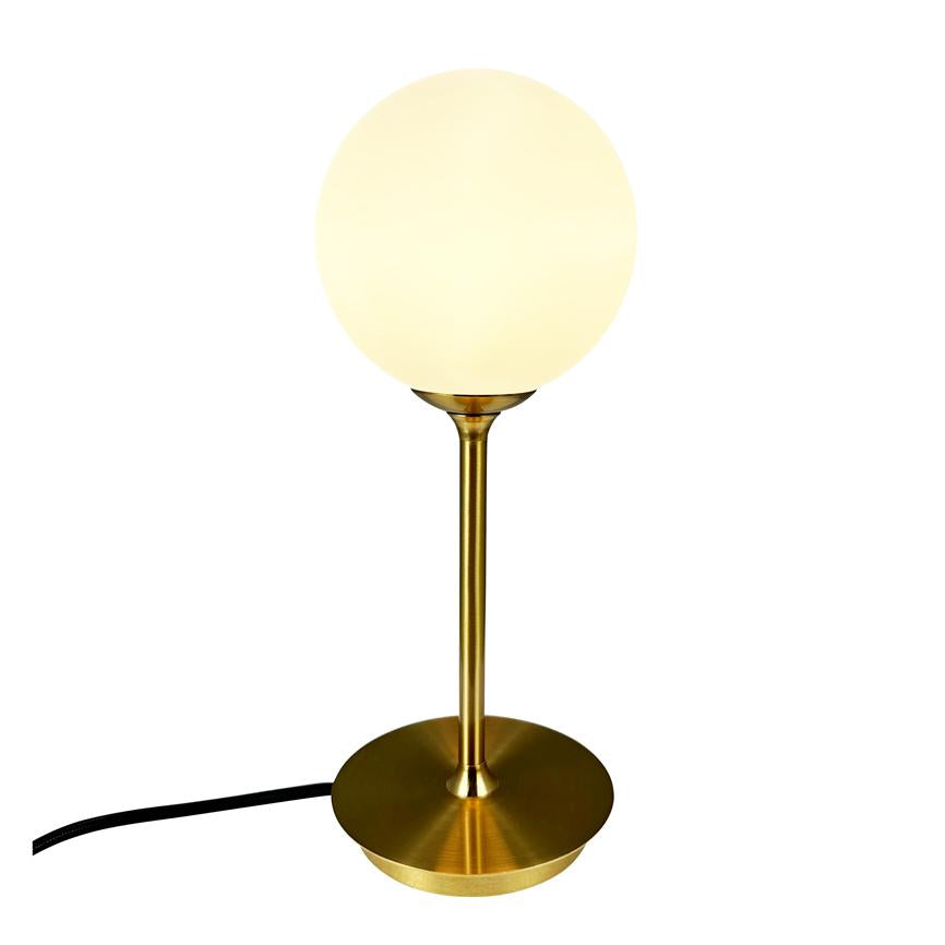 Table lamp with opal white ball shade, which emits warm light, mounted on slender brass rod and circular brass base; black power cable lies diagonally to the left on a white background.