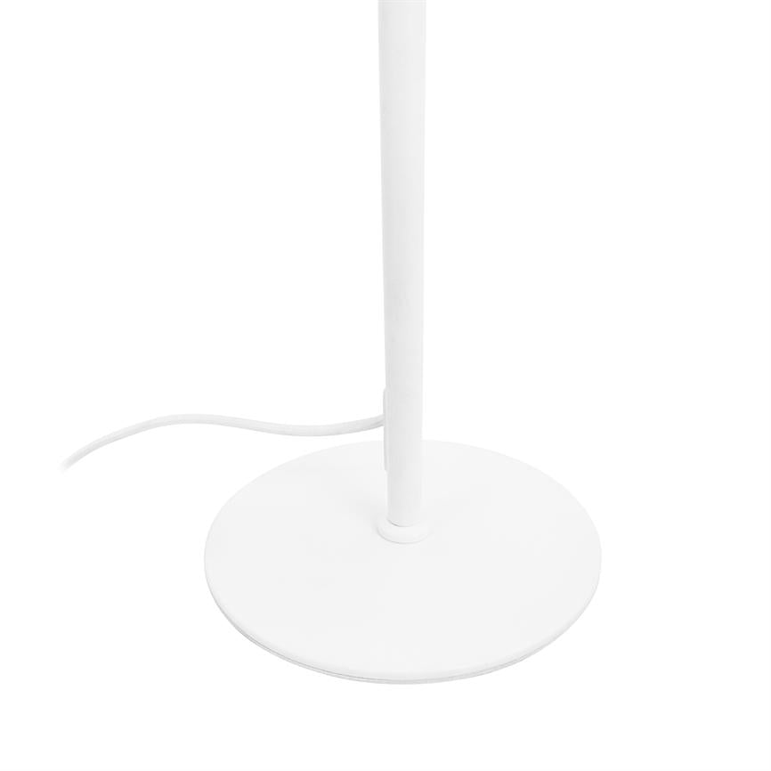 The lamp's round base stands on a white surface, its slim shaft extends upwards and a white cord bends out to the side in a bright, minimalist environment.