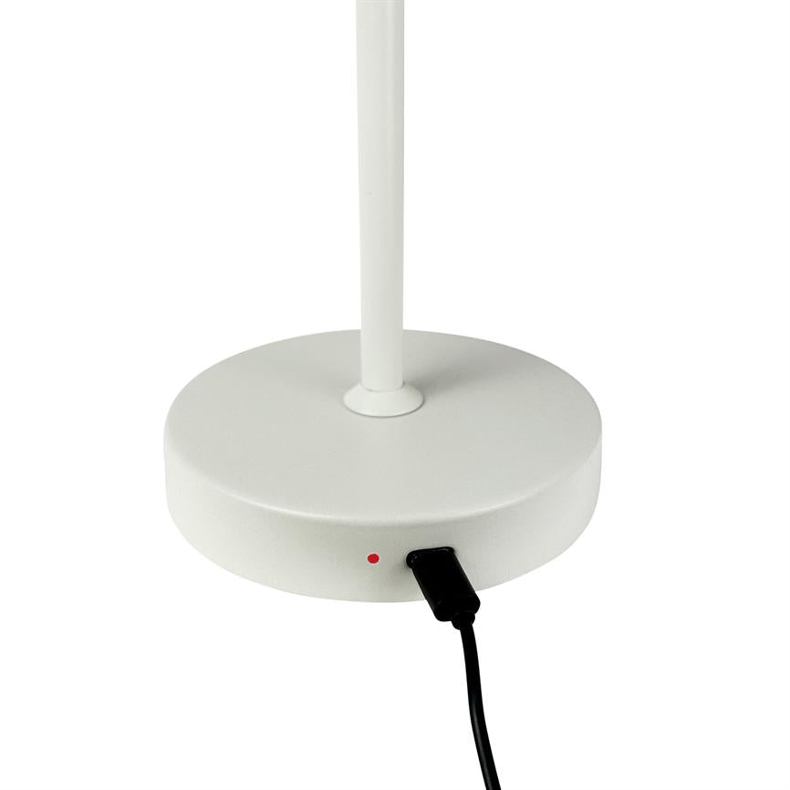 Round lamp base, a vertical lamp leg stands in the centre; a black USB cable is connected since a small red diode lights up; white minimal background.