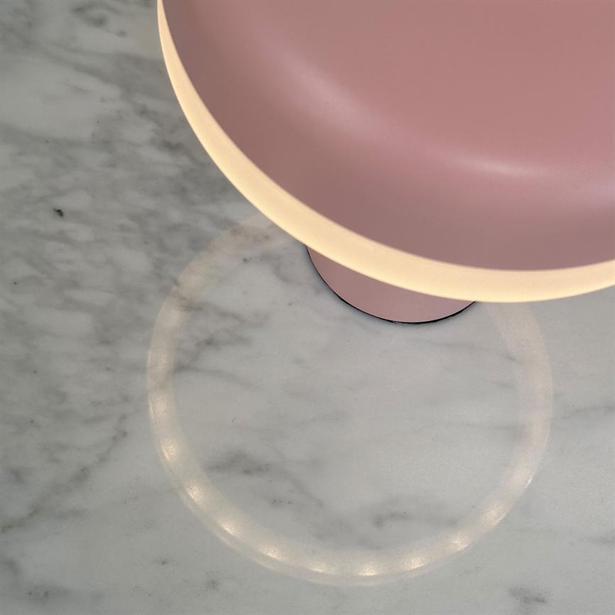Pink, bowl-shaped lamp (partially visible) casts a warm, ring-shaped light reflection on a white marble tabletop with faint veins.